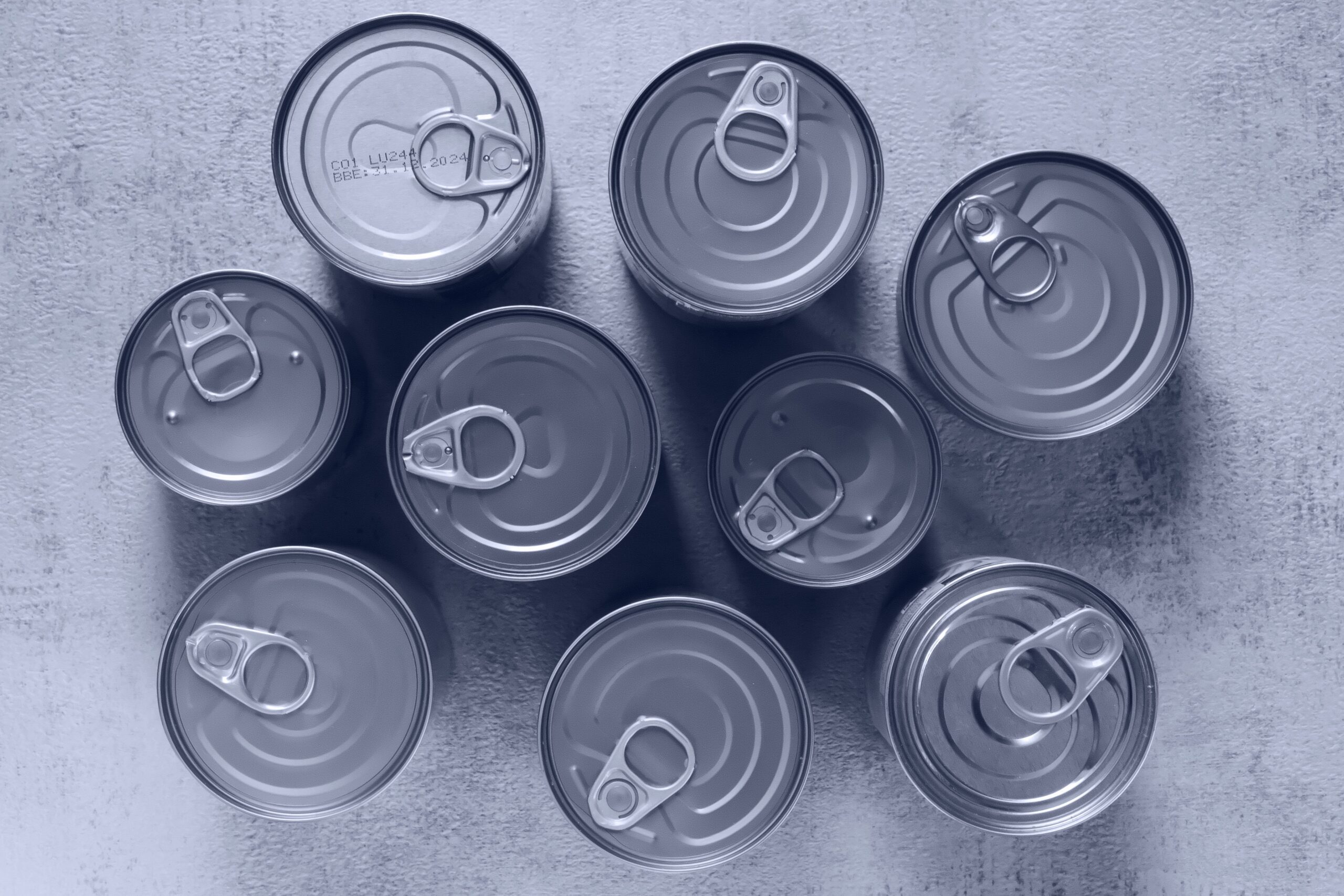 High-angle shot of canned food tins arranged on a rough surface, emphasizing texture and symmetry.